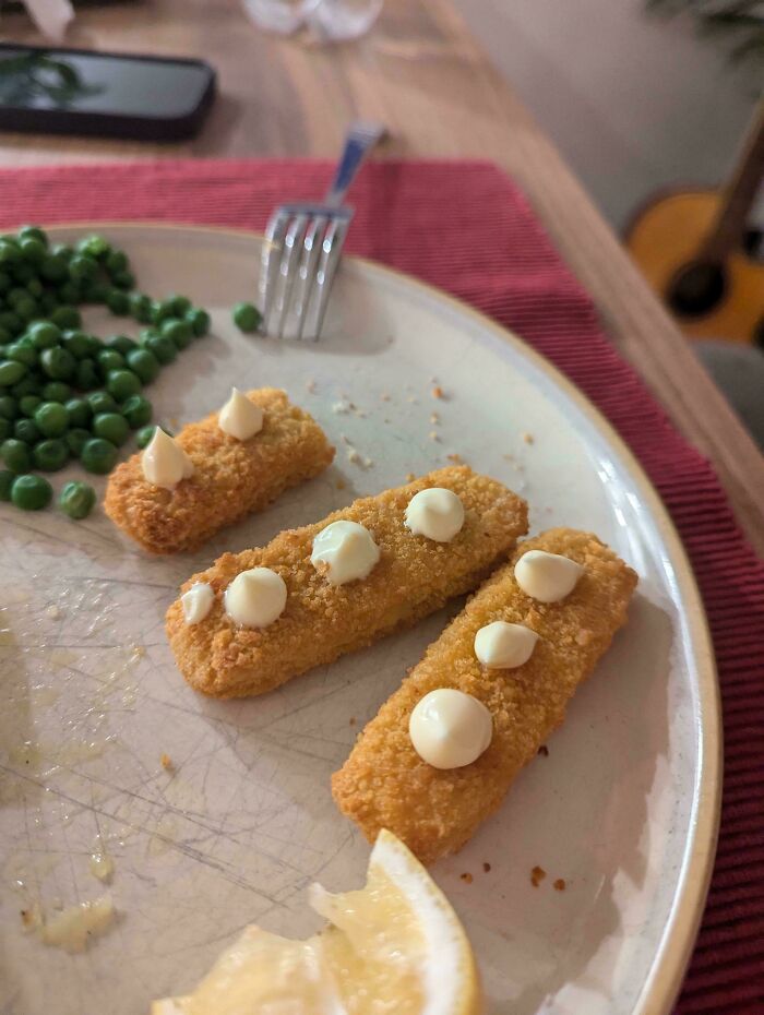 Fish sticks with dollops of sauce, peas, lemon slice on plate, offering mildly interesting detail.