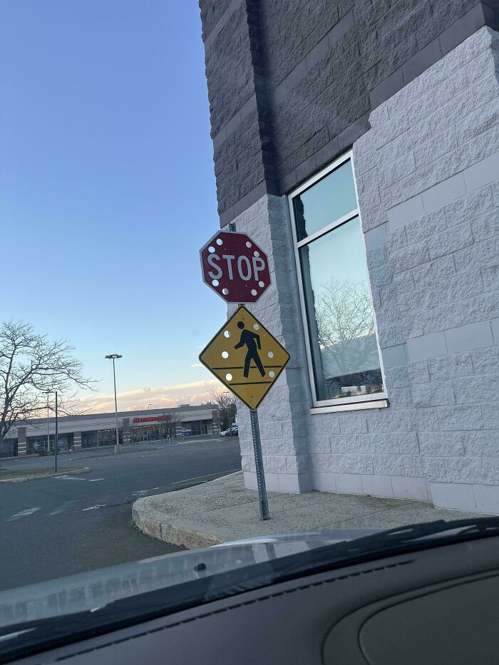 Mildly interesting stop sign with bulging dots and a pedestrian warning below, next to a building corner.