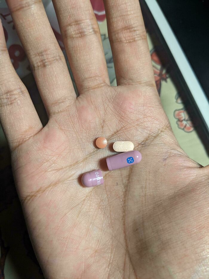 Hand holding three mildly interesting pills of different shapes and colors.