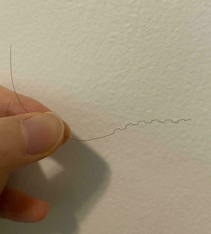 A person holding a zigzag-shaped hair in their fingers, showcasing a mildly interesting detail against a plain wall.