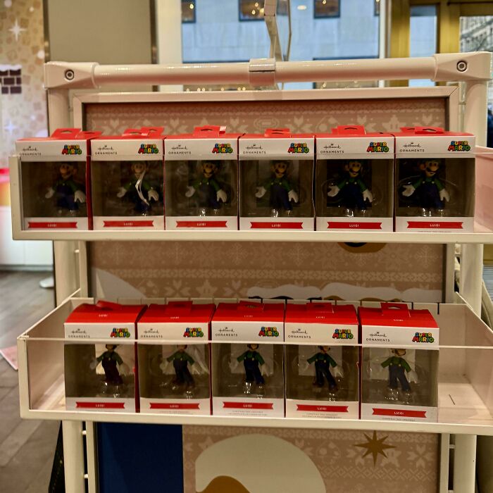Display of Luigi ornaments from Super Mario series, neatly arranged in boxes on a white shelf, offering mildly interesting amusement.
