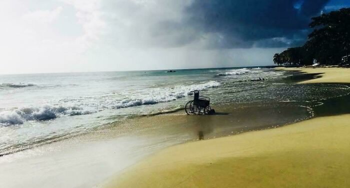 A wheelchair on a tranquil beach, waves gently lapping the shore under a cloudy sky, offering temperate amusement.