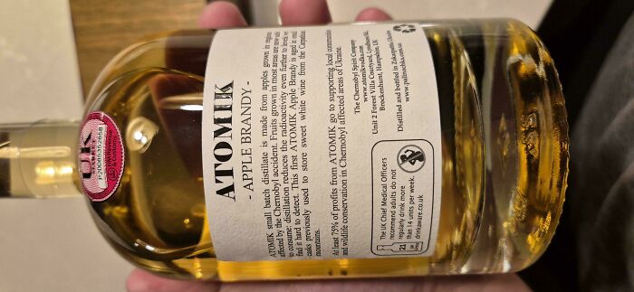 Hand holding a bottle of ATOMIK Apple Brandy with detailed label, mildly interesting for temperate amusement.