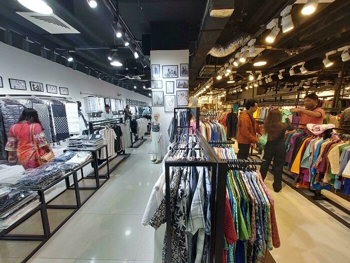 A clothing store aisle with various garments on racks, people browsing; mildly interesting shopping scene.