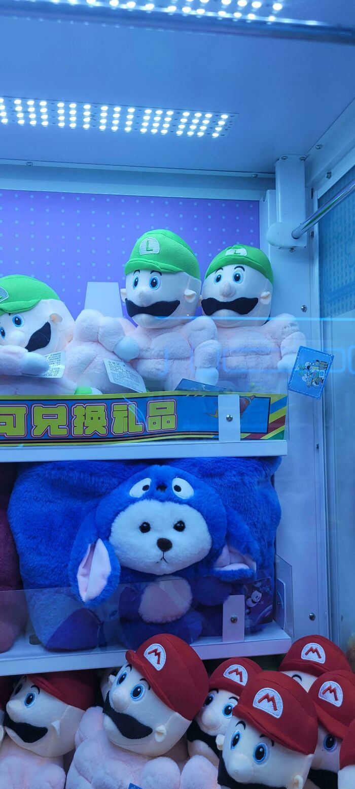 Claw machine filled with assorted plush toys featuring green and red-hatted characters for mildly interesting amusement.