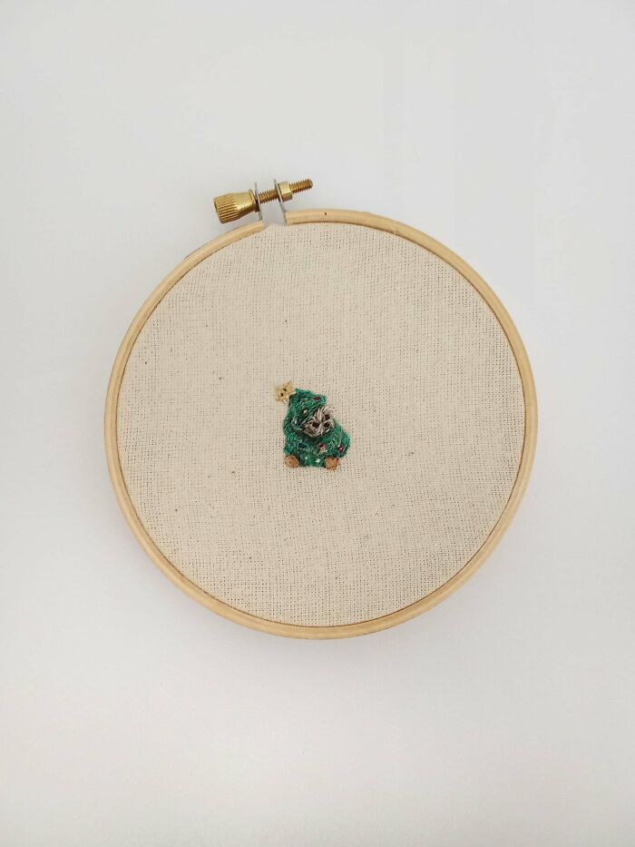 Small green embroidery design in a wooden hoop on beige fabric showcasing beautiful embroidery designs art.