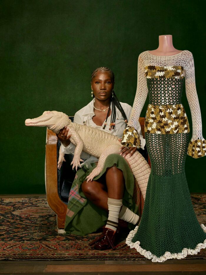 Woman holding a crocheted alligator next to a mannequin wearing a detailed green and floral crochet dress.