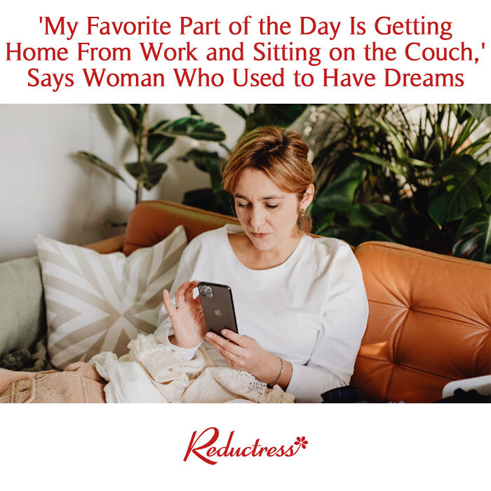 Woman sitting on a couch using a smartphone with funny fake article headline from Reductress online magazine visible.
