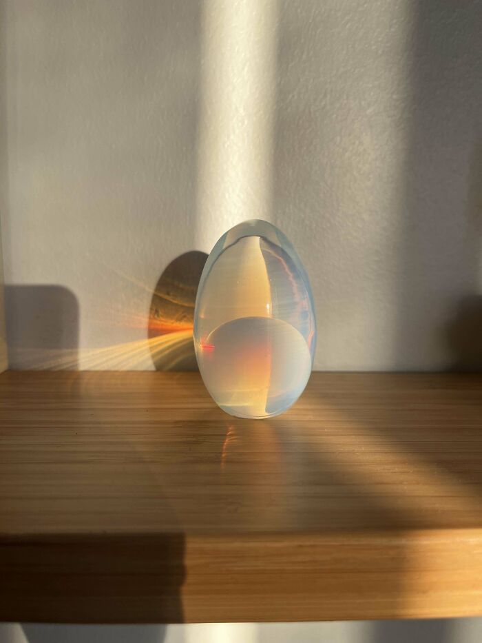 Glass egg with rainbow reflection on a wooden shelf, found while thrifting.
