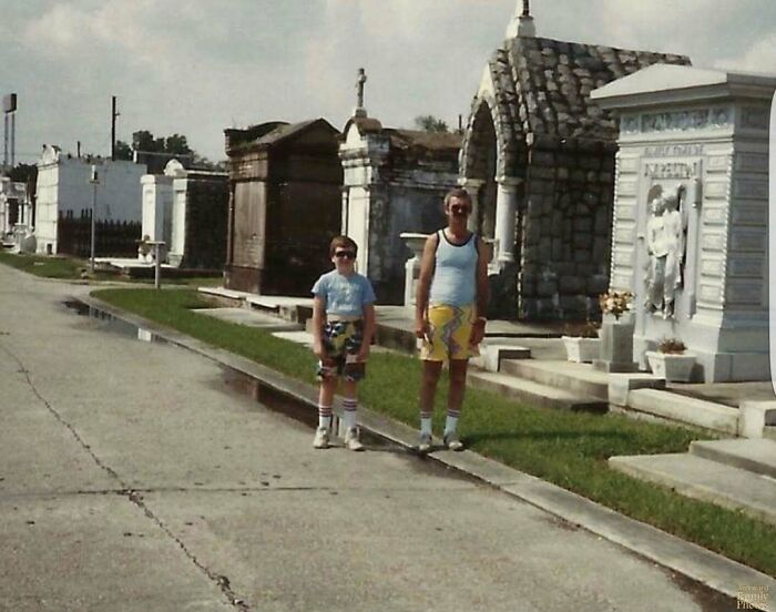 Awkward family photo of two people in a cemetery, wearing colorful shorts and sunglasses.