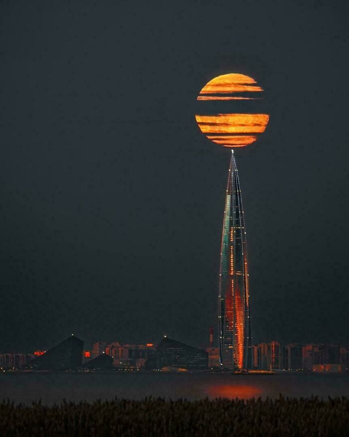 Massive full moon appearing above the tallest skyscraper at night, showcasing a scarily big natural phenomenon for megalophobia.