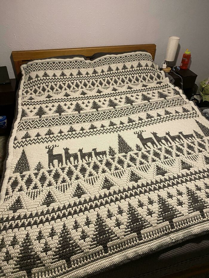 Crochet blanket featuring intricate patterns with trees and reindeer, showcasing a proud crochet enthusiast's project.
