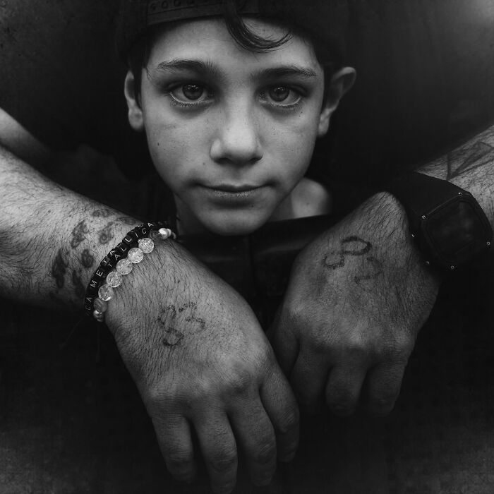 "Black-and-white portrait of a soulful boy by Lee Jeffries, featuring detailed tattoos and bracelets on his hands."