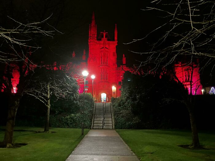 Historic building glowing red at night with dark trees, exuding an evil aura like a supervillain headquarters.