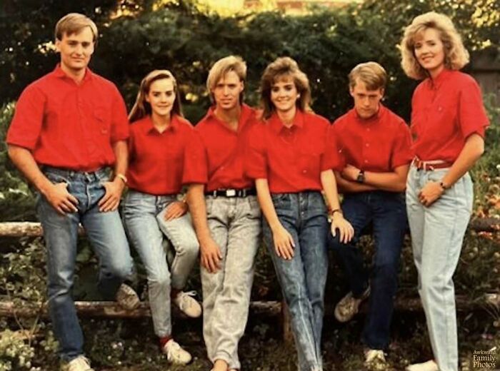 Awkward family photo with six people in matching red shirts and blue jeans posed outdoors.