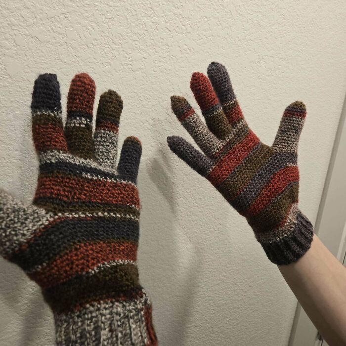 Handmade striped crochet gloves in earthy tones worn on both hands, showcasing a proud crochet enthusiast project.
