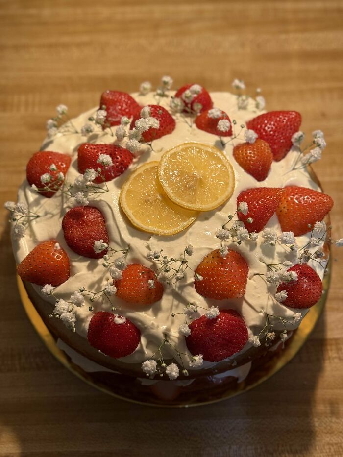 Artistic cake with strawberries, lemon slices, and delicate flowers, showcasing culinary skills at a whole other level.