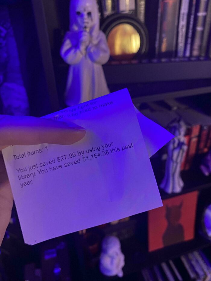 A library savings receipt against a backdrop of eerie figurines, highlighting consumerism critique.