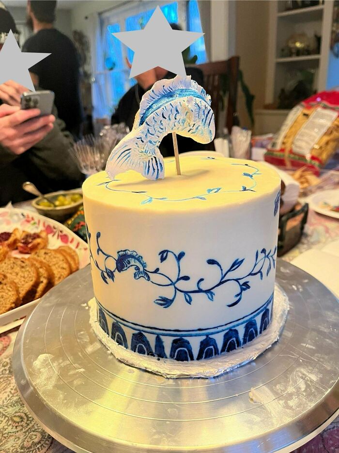 A beautifully decorated cake with intricate blue designs and a fish topper, showcasing a baker's culinary concoction.