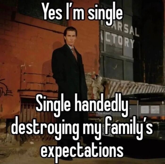 Man in a dark coat standing by a wall with a funny meme about being single and destroying family expectations.
