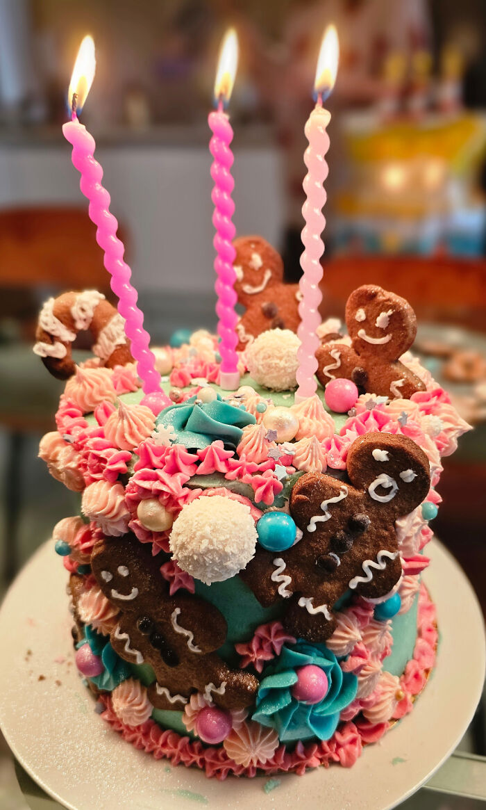 Colorful cake topped with gingerbread cookies and pink candles, showcasing bakers' culinary creations elevated to another level.