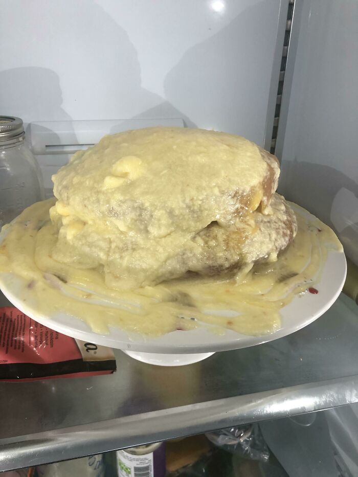Unhinged food: a collapsed cake with frosting melting off, resting on a plate in a refrigerator.