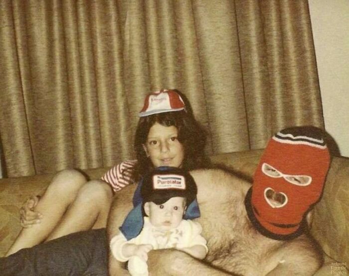 A family photo with three people on a couch; one in a ski mask, showcasing awkward family moments.