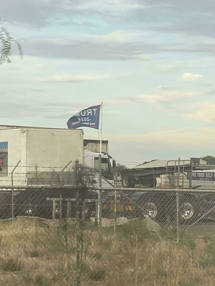 Australian truck with a "Trump 2024" flag parked behind a fence under a cloudy sky.
