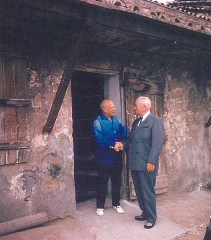 Two men in suits shaking hands outside an old rustic building, capturing a fascinating historical moment.
