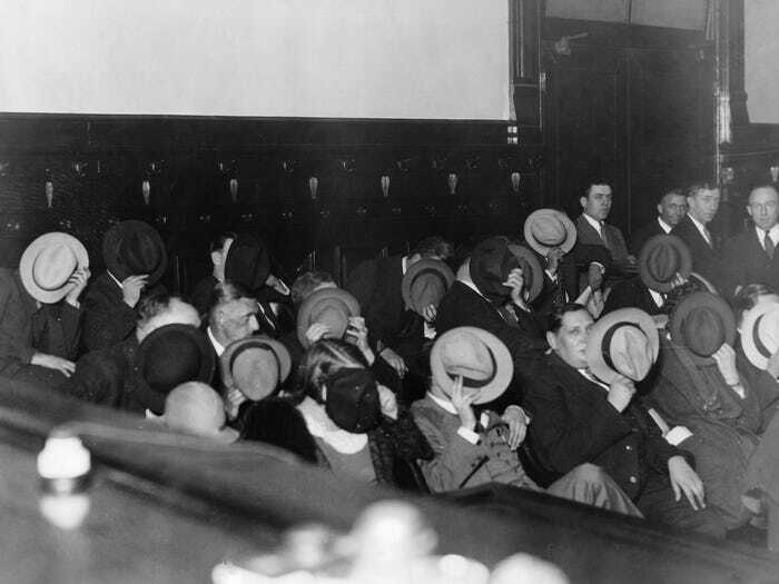 Group of people in historical attire sitting down, covering their faces with hats.