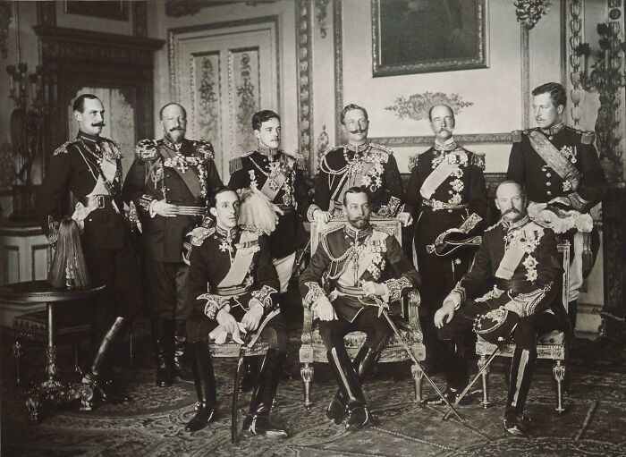 Group of royal figures in ornate uniforms, posing in a grand historical room.