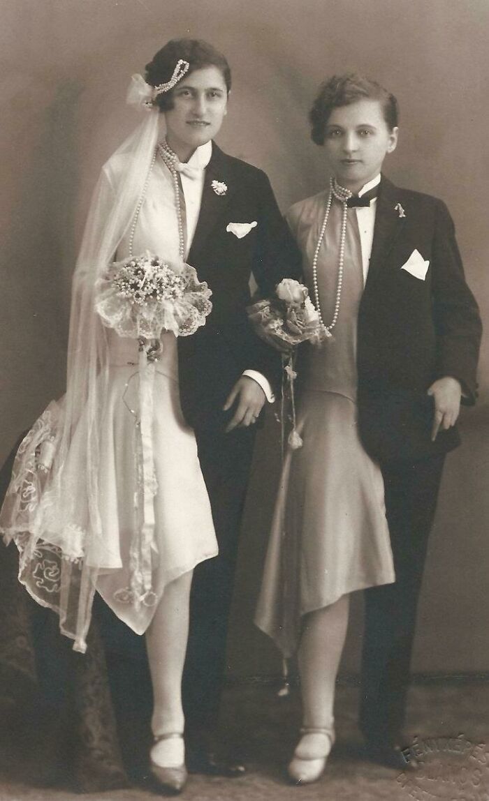 Vintage wedding photo of two women in suits and dresses, showcasing historical fashion.