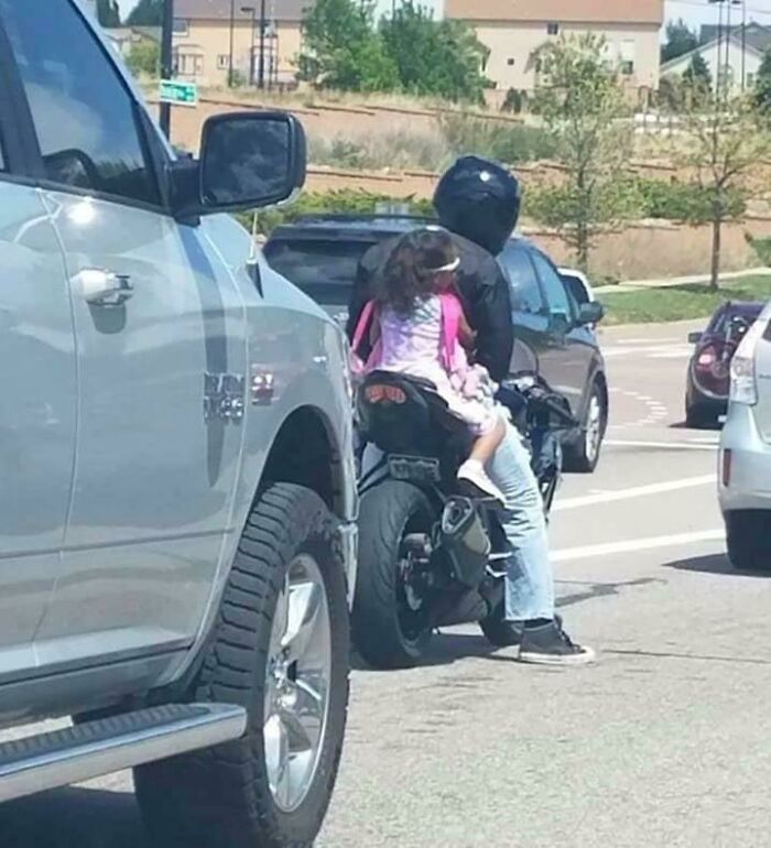 Child without helmet riding on motorcycle with parent, highlighting safety concerns.
