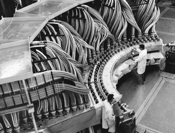 Factory workers assembling complex machinery with numerous cables; a fascinating historical pic.
