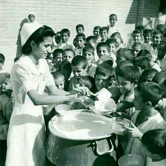 Nurse serving food to a group of smiling children in a historical setting, highlighting fascinating historical pics.