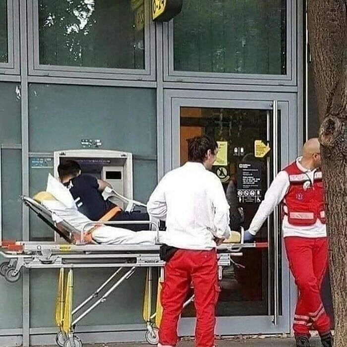 Two paramedics in red pants pushing a patient on a stretcher near a building with glass windows and a door.