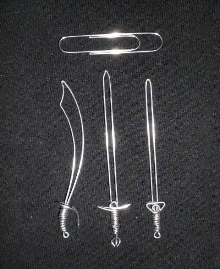 Three miniature swords crafted from paperclips, resembling album cover artwork, are displayed on a black background.