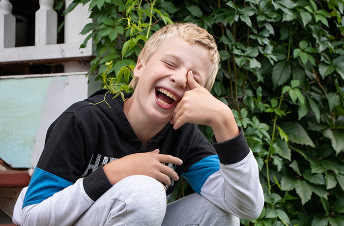 Teen laughing in a garden, wearing a black and blue hoodie with white pants, evoking a playful mood.