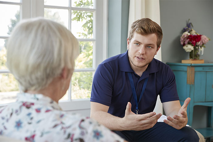Man in a blue shirt talking to an older woman in a floral blouse about wedding dress preferences.