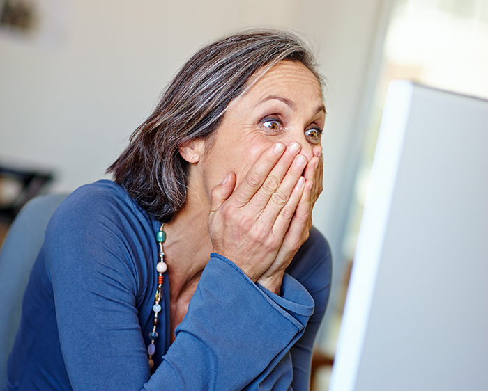 A surprised woman in front of a computer, reacting to a background check revelation.