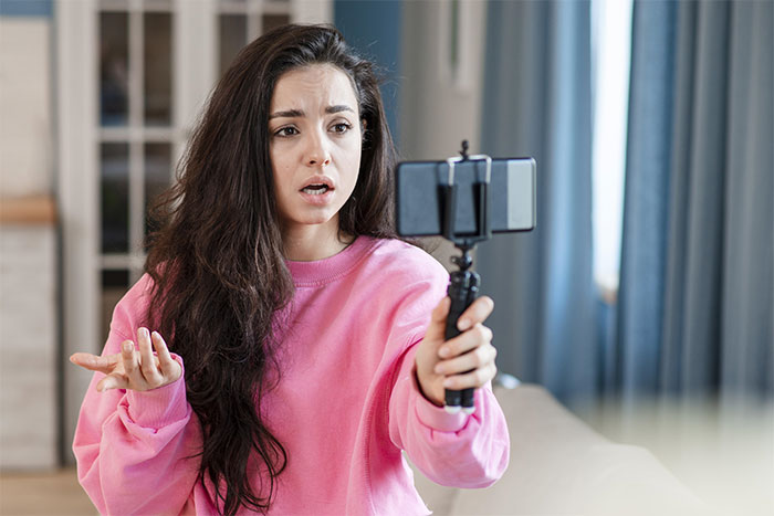 Woman in a pink sweater filming herself with a smartphone, discussing trading services. Woman in a pink sweater filming herself with a smartphone, discussing trading services.