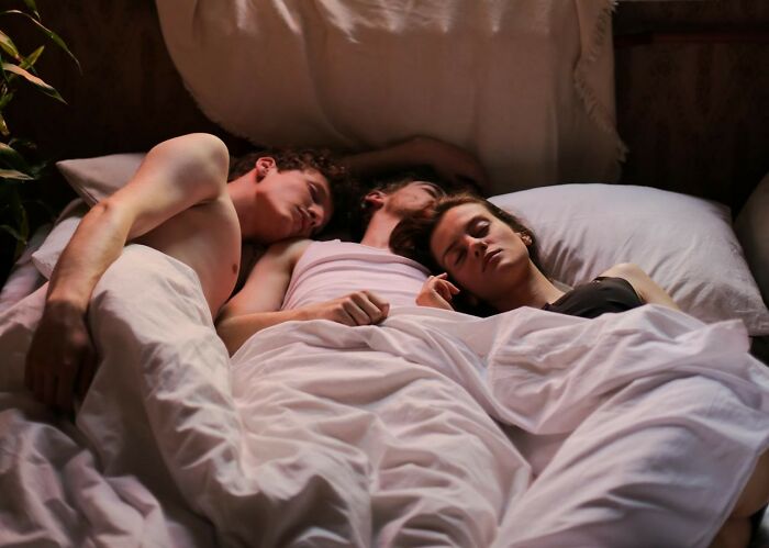 Three people sleeping in one bed after a wild work Christmas party, symbolizing post-potluck chaos.