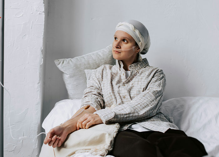 Person sitting on a bed with a pensive look, wearing a headscarf.