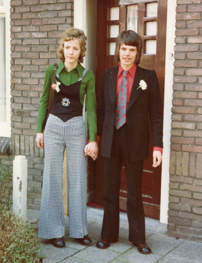 Couple in 1973 fashion, holding hands outside a brick building, reflecting World-In-Pictures theme.