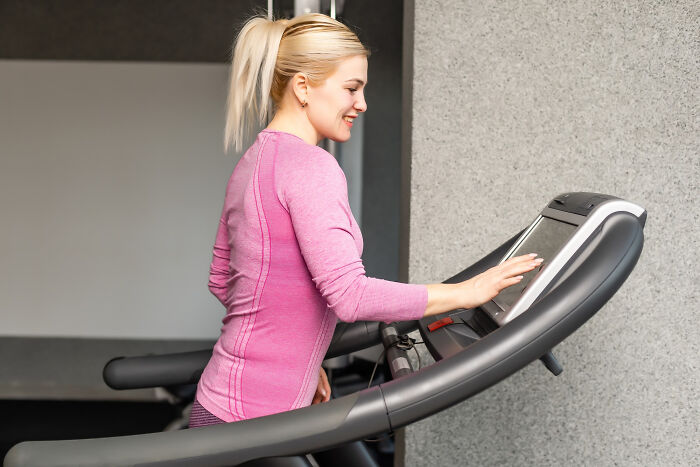 Woman in pink workout clothes on treadmill adjusting settings, focusing on fitness bonuses.
