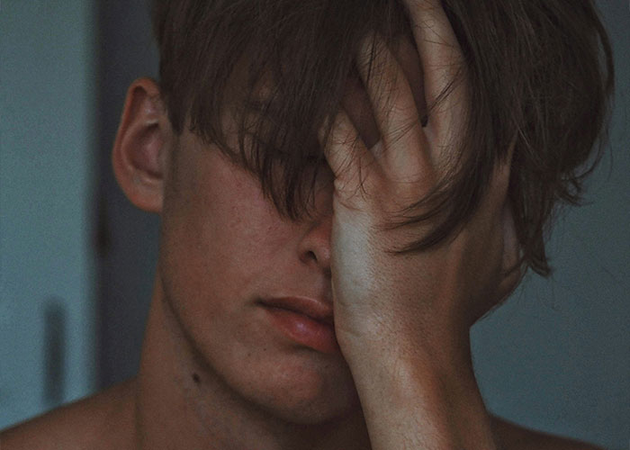 A person with tousled hair covering their face, symbolizing regret over spilled secrets.