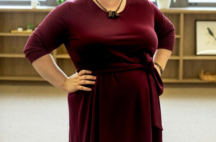 Person in a burgundy dress stands confidently with hands on hips, showcasing a moment of empowerment.
