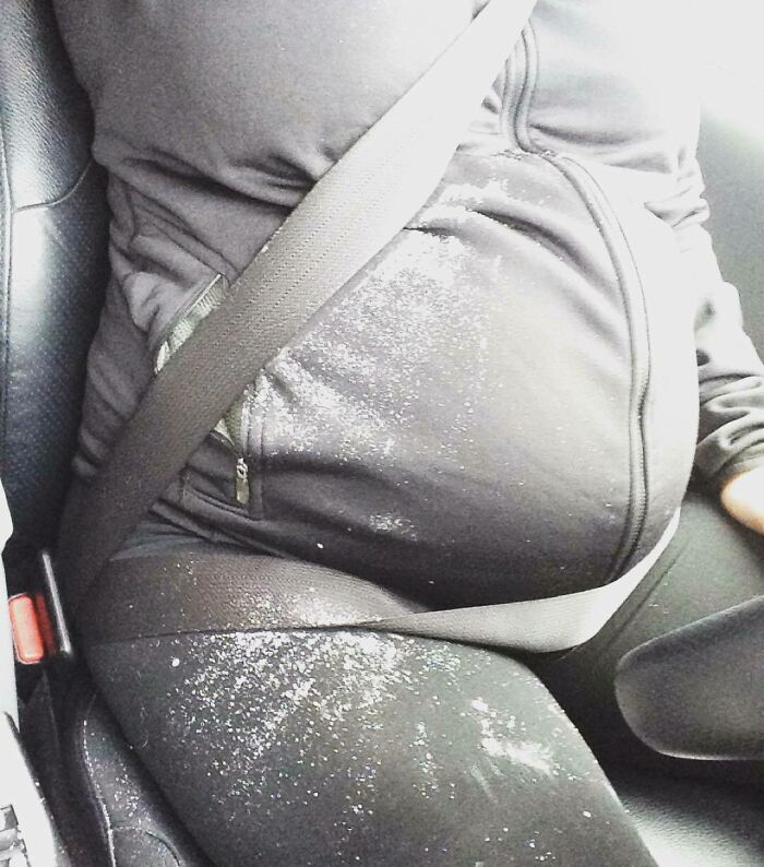 Pregnancy belly with spilled powder on black clothes in a car seatbelt, illustrating funny pregnancy situations.