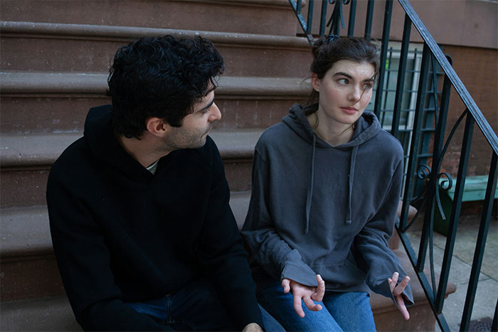 Two people sitting on stairs, engaged in a serious conversation about chores and gender roles.