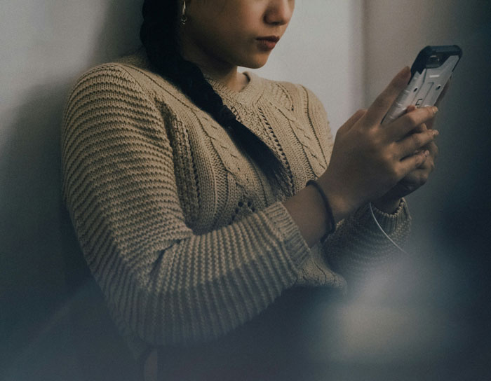Gen A individual using a smartphone, wearing a knitted sweater, focused on the screen.